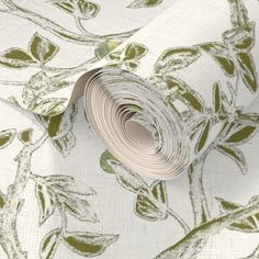 a roll of white and green floral wallpaper on top of a tablecloth with leaves