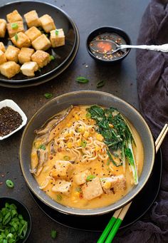 a bowl filled with noodles and tofu next to bowls of vegetables on a table