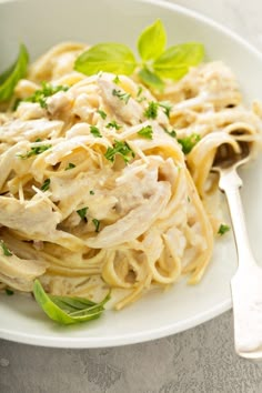 a white plate topped with pasta covered in sauce and parsley next to a fork