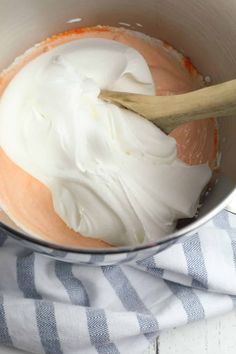 a bowl filled with whipped cream on top of a blue and white striped towel next to a wooden spoon