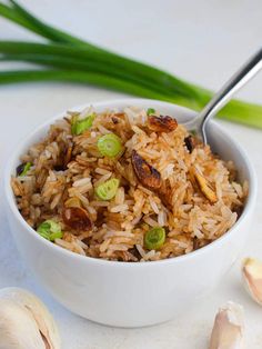 a white bowl filled with rice and vegetables next to some garlic on a table top