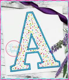 an appliqued letter is shown on a piece of paper with purple ribbon