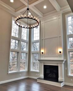 an empty living room with large windows and a chandelier hanging from the ceiling