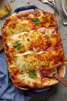 a casserole dish with meat and cheese in it on a blue cloth next to utensils