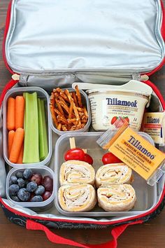 an open lunch box filled with fruit, vegetables and pretzel sticks on top of a wooden table