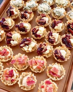 many small pastries are arranged on a baking sheet with cranberry sauce and pecans