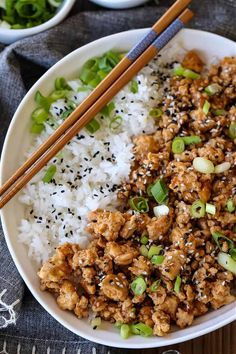 a white bowl filled with rice and meat next to chopsticks