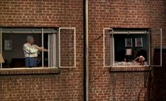 two men looking out the windows of a brick building