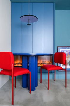 two red chairs sitting in front of a blue table with a fire place next to it