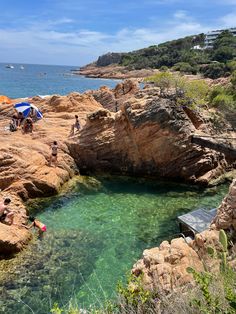 people are swimming in the clear blue water near some rocks and trees on the shore