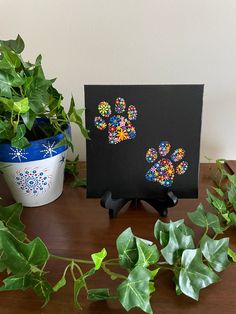 a black card with colorful dog paw prints on it next to some green plants and a potted plant