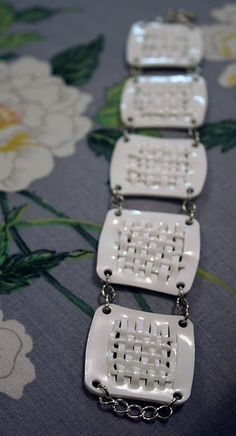 four white necklaces are sitting on a flowered tablecloth with flowers in the background