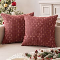 two red pillows sitting on top of a couch next to a christmas tree with pine cones