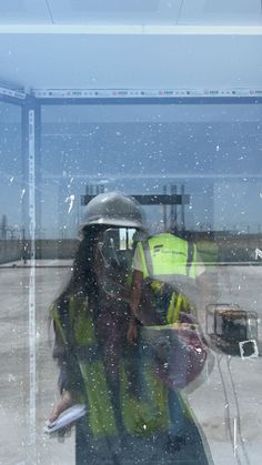 a woman in yellow vest and hard hat standing next to a window