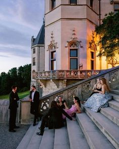 several people sitting on the steps in front of a building at dusk with one person taking a photo