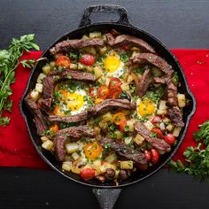 an iron skillet filled with steak, potatoes and vegetables on top of a red towel