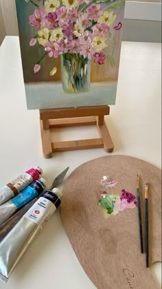 an easel with paint and flowers on it sitting next to some other art supplies