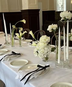 the table is set with white flowers and black ribbon napkins, candles, and plates