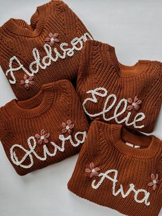 three knitted sweaters with embroidered name and flowers on the front, two are brown