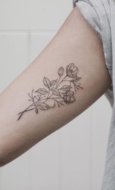 a black and white photo of a flower tattoo on the left arm, with leaves around it