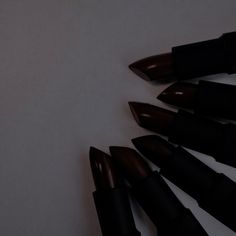 six black lipsticks lined up in a circle on a white surface, with one being pointed at the camera