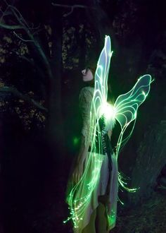 a woman is standing in the dark with her arms spread out and lights projected on her body