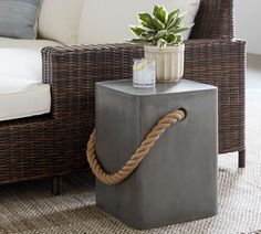 a rope wrapped end table with a potted plant on it and a wicker sofa in the background