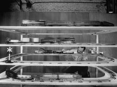 a black and white photo of a man working on a model train set in a building