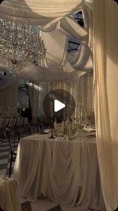 a table is set up with white linens and chandeliers