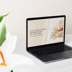 an open laptop computer sitting on top of a white desk next to a flower vase