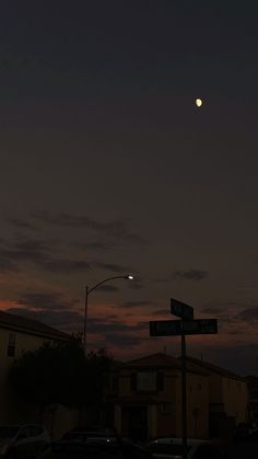 the moon is setting over some houses and street signs