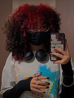 a woman with red hair wearing a black mask and holding a cell phone in her hand