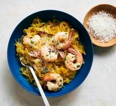 a blue bowl filled with shrimp and rice next to a wooden spoon on a white surface