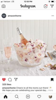 a glass bowl filled with ice and flowers next to two wine glasses on a table