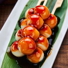 there are jelly balls on a green leaf with spoons in it and sauce over them