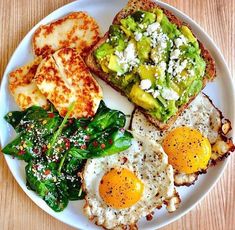 a white plate topped with eggs and toast next to spinach on top of a wooden table