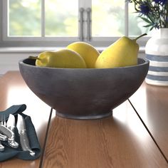 a bowl filled with lemons and two pears on top of a wooden table