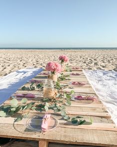 a table set up on the beach with flowers in vases and napkins laid out