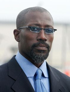 a man wearing glasses and a suit with a blue tie is looking at the camera