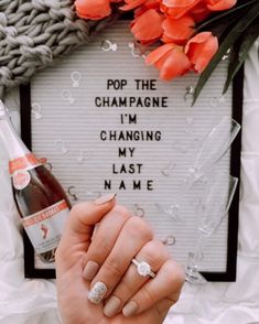 a woman is holding her wedding ring in front of a sign that says pop the champagne i'm changing my last name