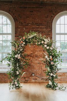 an arch decorated with flowers and greenery in front of two windows