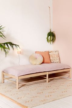 a pink daybed with pillows on it in a white room next to a potted plant