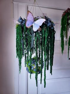 a hanging planter with moss and butterflies on it's sides, in front of a white door