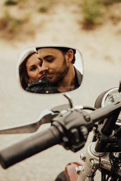 a man and woman are reflected in the side mirror of a motorcycle