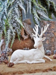 a white deer figurine sitting in front of a potted plant with snow on it