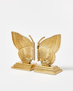 two golden butterfly figurines sitting side by side on top of each other in front of a white background