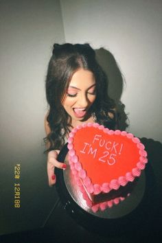 a woman holding a heart shaped cake with the words f k i m e s on it