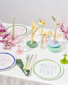 a table topped with plates and vases filled with flowers next to candles on top of a white table cloth