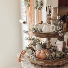 a three tiered tray with pumpkins, greenery and other items on it