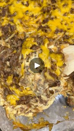 a casserole dish with meat and cheese on it, being stirred by a wooden spatula